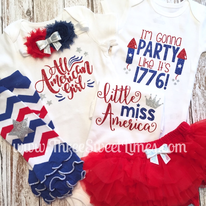 May include: Two white onesies with red, white, and blue glitter text. One says "All American Girl" and the other says "I'm Gonna Party Like It's 1776!"  A red tutu with a silver bow, a pair of red, white, and blue striped leg warmers, and a headband with a red, white, and blue bow are also included.