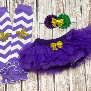 May include: Purple and white chevron leg warmers with gold fleur-de-lis accents, a purple tulle tutu with a yellow bow, and a purple and green flower headband with a yellow bow.