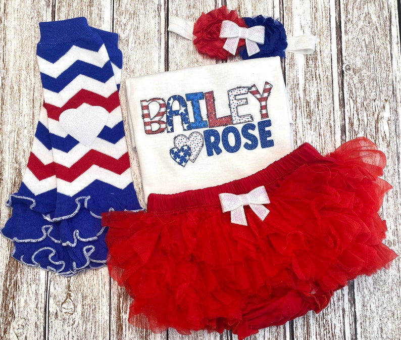 May include: Red, white, and blue baby outfit with a ruffled skirt, leg warmers, and a headband. The shirt has the name "BAILEY ROSE" in glittery letters with a red, white, and blue heart.