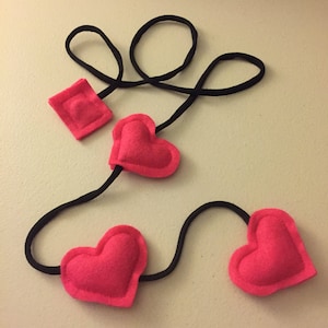 May include: A black string with three pink felt hearts attached. The hearts are in different shapes and sizes.