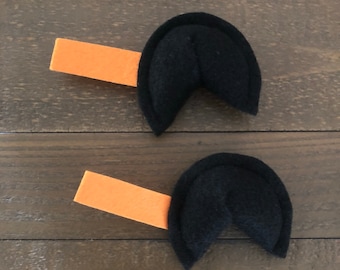 May include: Two black felt fortune cookie shapes with orange felt strips attached to the back.