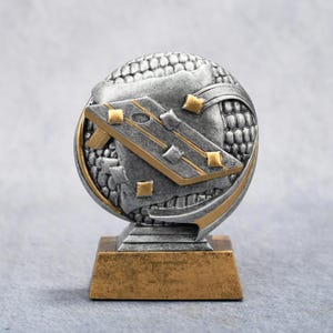 May include: A silver and gold trophy with a detailed design. The trophy features a round, textured top with a gold and silver design, and a rectangular gold base. The design includes gold accents and a geometric pattern.