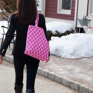 May include: A pink tote bag with a white quatrefoil pattern is carried over the shoulder. The bag is held by a person wearing a black blazer, black pants, and black boots. The bag is from Georgia Totes.