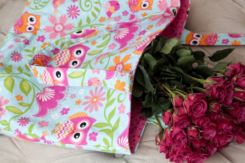 May include: A light blue tote bag with a colorful owl and floral pattern. The bag has a pink interior and a matching strap. A bouquet of red roses is placed inside the bag.