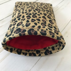 May include: A small, leopard print pouch with a red lining. The pouch is made of fabric and has a zipper closure.