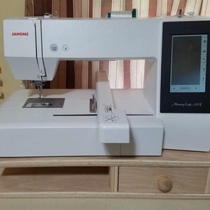 May include: White Janome Memory Craft 500E embroidery machine with a built-in screen, sitting on a wooden stand with a drawer.