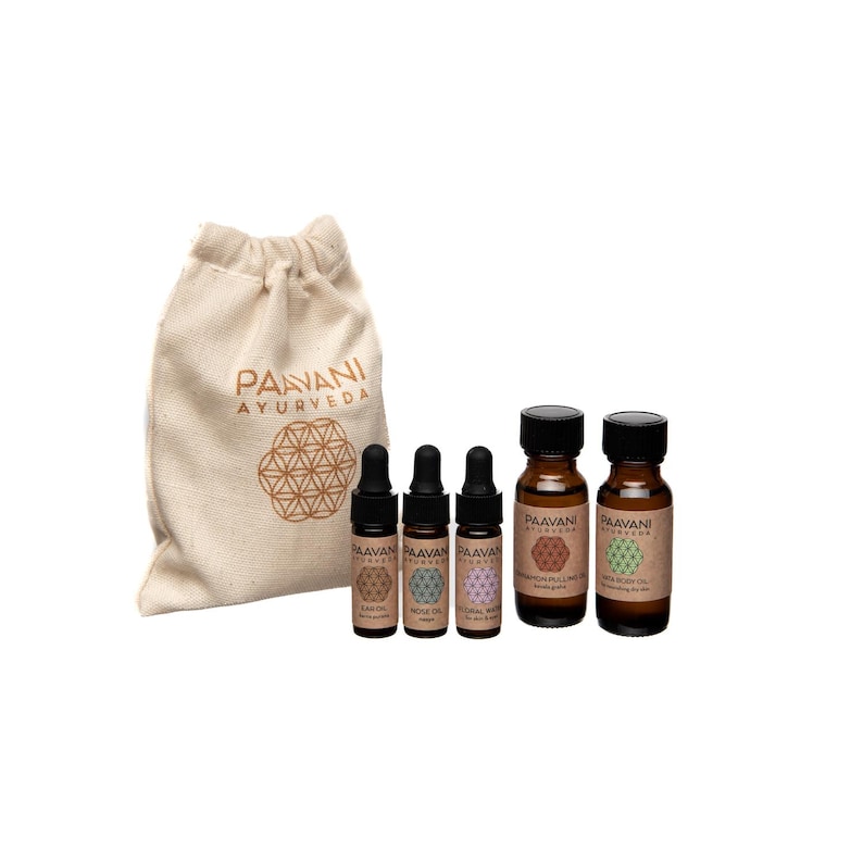 Op de afbeelding: Set van vier kleine bruine glazen flesjes met etiketten waarop "Paavani Ayurveda" staat en die etherische oli&euml;n bevatten. De flesjes zitten in een kleine witte canvas tas met hetzelfde logo.