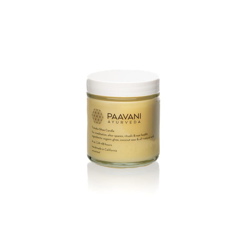 May include: A small glass jar with a white lid containing a yellow candle. The jar has a label that reads "Paavani Ayurveda" and "Tattva Ghee Candle". The candle is for meditation, altar spaces, rituals, and eye health. The ingredients are organic ghee, coconut wax, and all-natural essential oils. The candle burns for 24-48 hours. It is handmade in California.