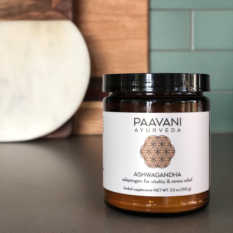 Puede incluir: Un frasco de vidrio marr&oacute;n con tapa negra que contiene suplemento herbal de Ashwagandha. La etiqueta es blanca con texto negro y un dise&ntilde;o de mandala marr&oacute;n. El texto dice "PAAVANI AYURVEDA ASHWAGANDHA adapt&oacute;geno: para vitalidad y alivio del estr&eacute;s suplemento herbal NET WT. 3.5 oz (100 g)"