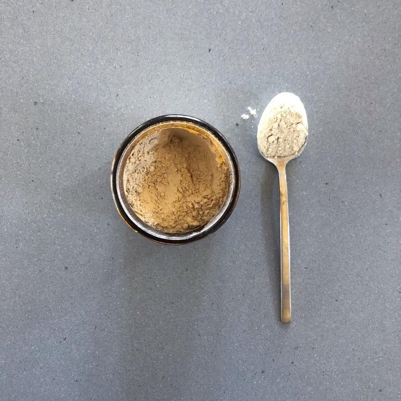 May include: A small glass jar filled with a light brown powder, and a silver spoon with a small amount of the powder on it.