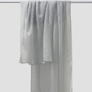 May include: A light gray, textured scarf is draped over a white bar. The scarf has a ribbed pattern and a slight sheen, creating a flowing, elegant appearance. The fabric is lightweight and appears to be soft. The scarf is a versatile accessory.