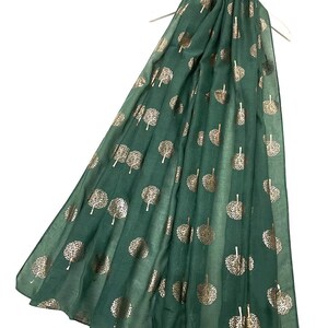 Peut inclure: Écharpe vert foncé ornée d'un motif de feuilles d'or. Le tissu fluide est mis en valeur sur un cintre blanc. Les arbres stylisés présentent des branches détaillées et des couronnes circulaires, créant un motif décoratif.