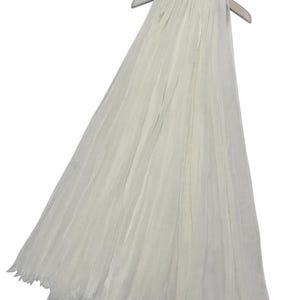 Può includere: Una sciarpa bianca di chiffon con un bordo a frangia. La sciarpa è appesa a un appendiabiti.