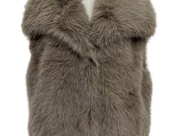 May include: A faux fur vest in a neutral taupe color. The vest features a wide, shawl-style collar and a soft, textured appearance. The sleeveless design and plush material suggest a focus on warmth and style.