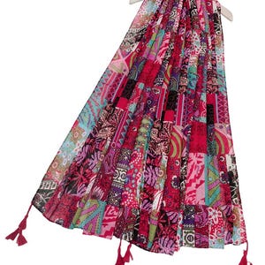 Può includere: Una sciarpa rosa, verde e blu con frange. La sciarpa è realizzata in un tessuto leggero e ha un design patchwork.