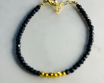 Peut inclure: Un bracelet en perles noires avec un accent doré. Le bracelet est composé de petites perles rondes et possède un fermoir simple.