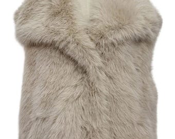 May include: A light beige faux fur vest with a wide collar. The vest is displayed on a mannequin and has a soft, textured appearance. The neutral color makes it a versatile layering piece.