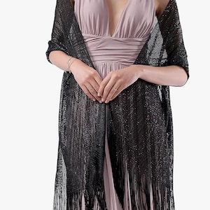 May include: A black, sparkly shawl with a fringed hem. The shawl is worn over a pale pink dress. The fabric of the shawl looks lightweight and possibly sheer, designed to be worn over the shoulders as an accessory.