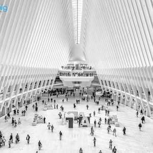 May include: A black and white photo of a large, modern building with a white, geometric ceiling and many white beams. The building is filled with people walking around. The building is very bright and airy.