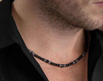 May include: A black beaded necklace with silver accents. The necklace is made of small, round beads and is worn by a person.