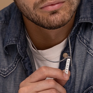 Könnte beinhalten: Eine silberne Kettenkette mit einem silbernen Barrenanhänger, der mit der römischen Zahl 'VII.XII.VIIA' graviert ist.