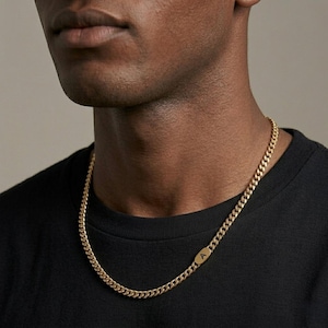 May include: A gold-toned curb chain necklace featuring a small, smooth, oval-shaped pendant integrated into the chain links. The pendant is engraved with the capital letter A in a clean, dark, sans-serif font, resting against a black t-shirt.