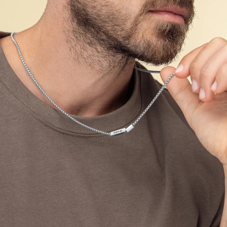 Puede incluir: Un collar de cadena de plata con un peque&ntilde;o colgante rectangular que dice "Tamar".