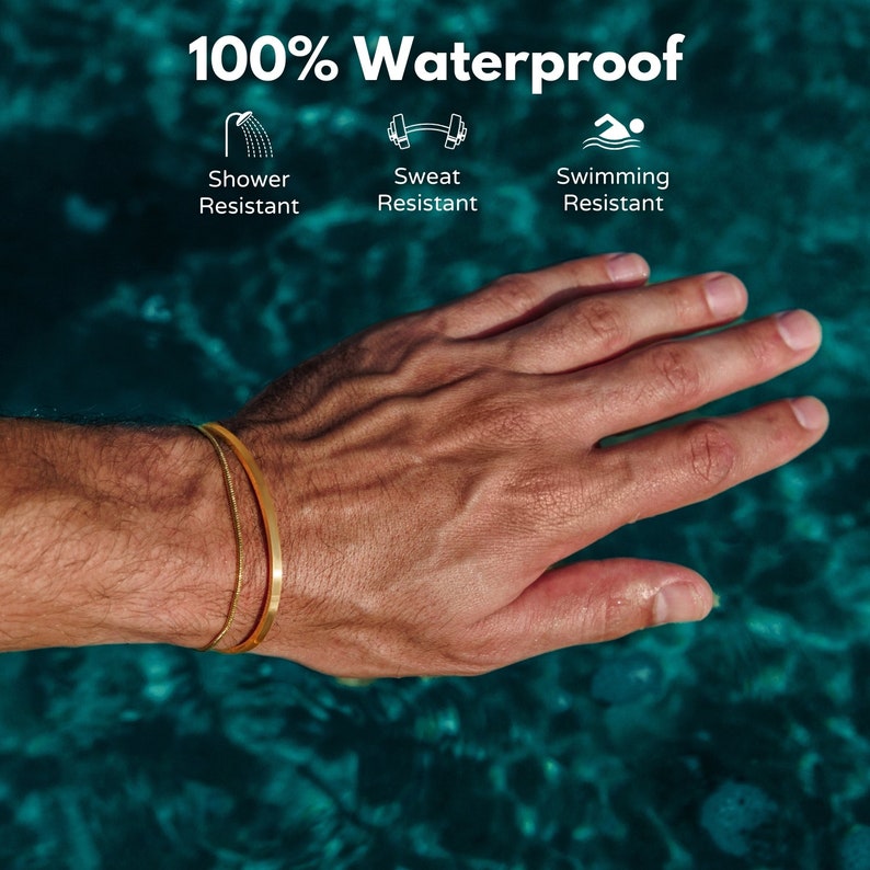 May include: A close-up of a hand wearing two gold bracelets. The bracelets are a thin, flat band and a delicate chain. The text "100% Waterproof" is at the top, with icons indicating shower, sweat, and swimming resistance.