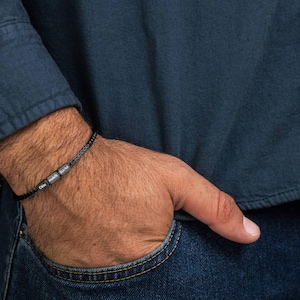 May include: A black braided bracelet with silver beads that spell out the names "Chloe" and "Jack" on a person's wrist.