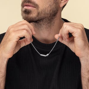 May include: A silver chain necklace with a small rectangular pendant. The pendant has a textured surface.