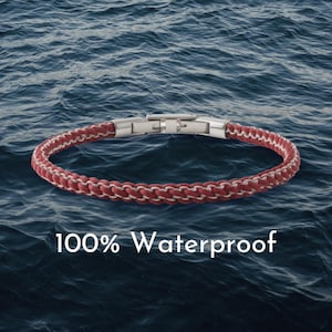 May include: Red and white braided bracelet with a silver clasp. The bracelet is shown against a backdrop of blue water. The text "100% Waterproof" is displayed in white.