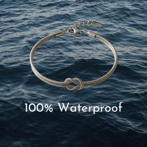 May include: Silver-toned bracelet with a knot design, set against a backdrop of blue water. The bracelet is made of a woven material and features a clasp closure. Text on the image reads "100% Waterproof".