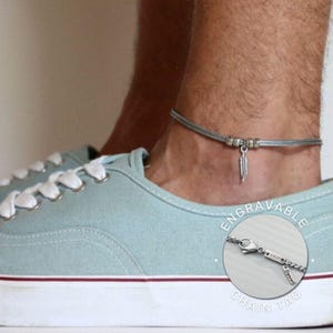 May include: A silver ankle bracelet with a feather charm and a small silver tag that says "Engravable Chain Tag". The tag is engraved with the name "Daniel".