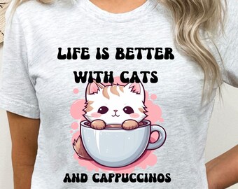 Könnte beinhalten: Ein graues T-Shirt mit einer niedlichen Comic-Katze in einer Kaffeetasse. Der Text auf dem T-Shirt lautet "Life is better with cats and cappuccinos."