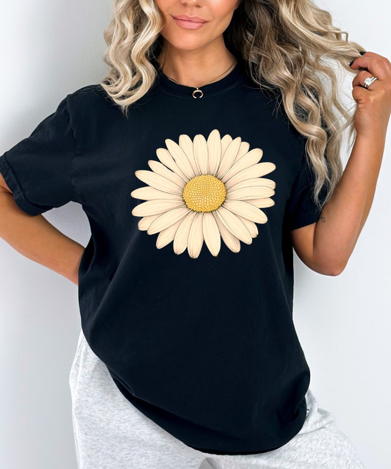 Puede incluir: Camiseta negra de gran tama&ntilde;o con un gran estampado de margarita blanca.