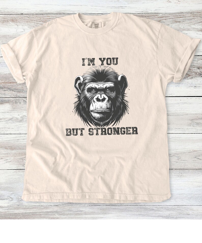 Peut inclure: Un t-shirt beige avec une illustration en noir et blanc d'un visage de singe et le texte "I'm you but stronger".
