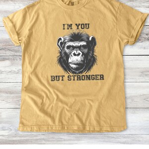 Peut inclure: Un t-shirt jaune moutarde avec une illustration en noir et blanc d'un visage de singe. Le texte "I'm you but stronger" est imprim&eacute; sous l'image.
