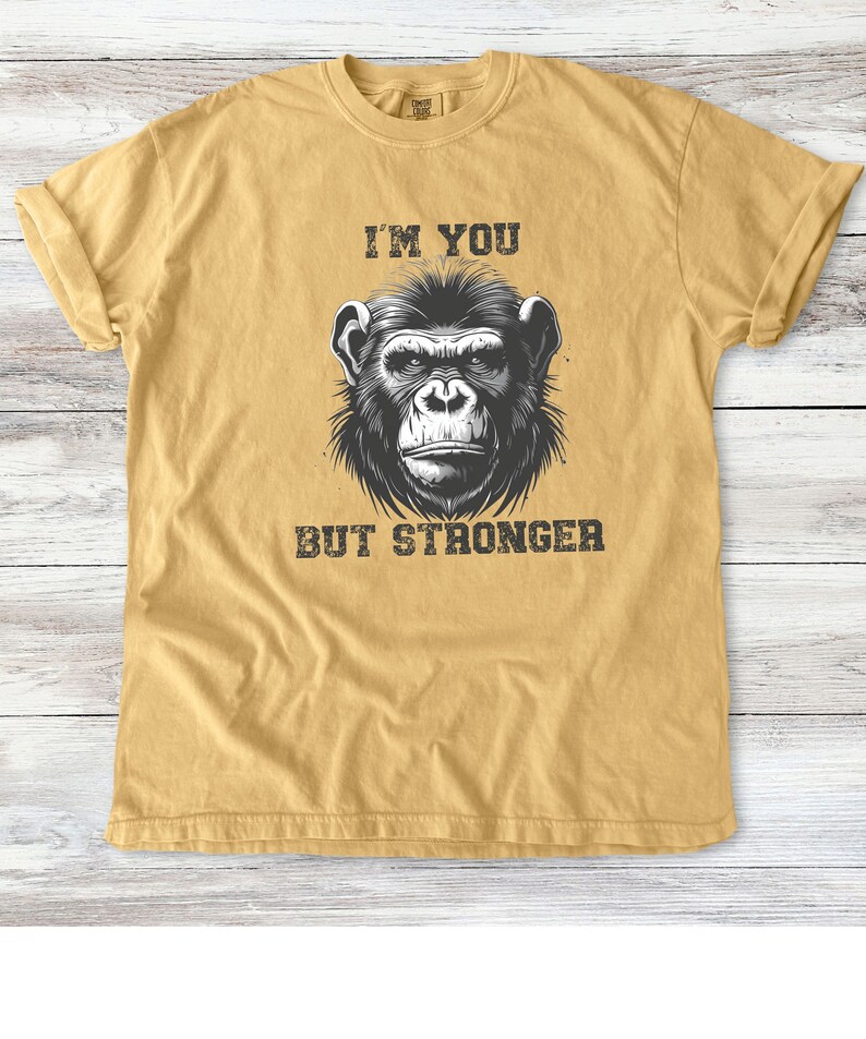 Peut inclure: Un t-shirt jaune moutarde avec une illustration en noir et blanc d'un visage de singe. Le texte "I'm you but stronger" est imprim&eacute; sous l'image.