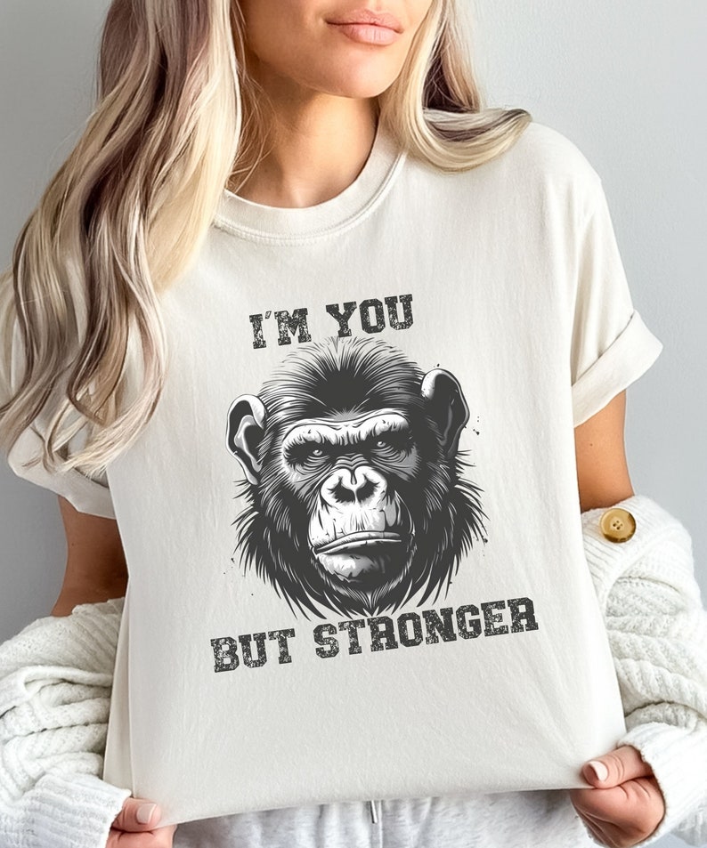 Peut inclure: Un t-shirt blanc avec une illustration en noir et blanc d'un visage de singe. Le texte "I'M YOU BUT STRONGER" est imprim&eacute; sous l'image.