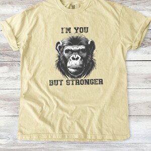 Peut inclure: Un t-shirt jaune clair avec une illustration en noir et blanc d'un visage de chimpanz&eacute;. Le texte "I'm you but stronger" est imprim&eacute; sous l'image.
