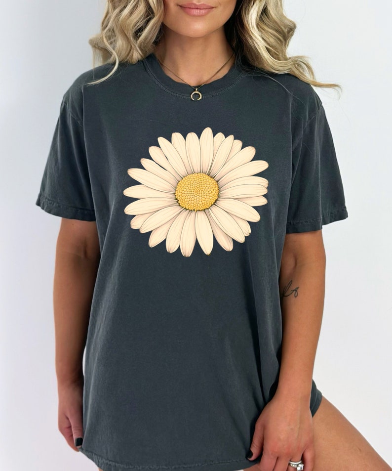 Puede incluir: Una camiseta gris oscuro con un gr&aacute;fico de margarita blanca. La margarita tiene un centro amarillo y p&eacute;talos blancos.