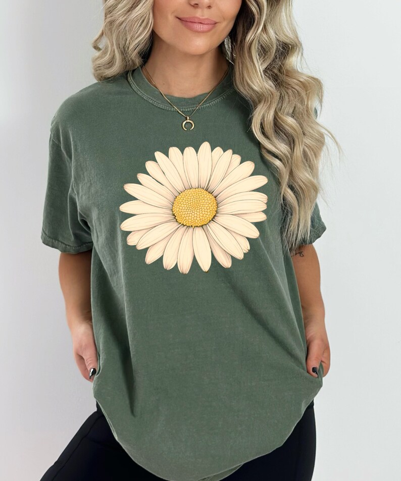 Puede incluir: Una camiseta verde con un gr&aacute;fico de margarita blanca. La margarita tiene un centro amarillo.