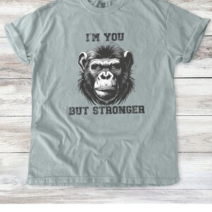 Peut inclure: Un t-shirt bleu clair avec une illustration en noir et blanc d'un visage de chimpanz&eacute;. Le texte "I'm you but stronger" est imprim&eacute; sous l'image.