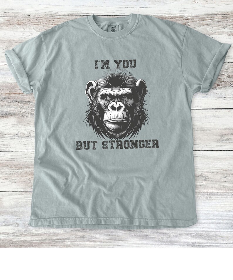 Peut inclure: Un t-shirt bleu clair avec une illustration en noir et blanc d'un visage de chimpanz&eacute;. Le texte "I'm you but stronger" est imprim&eacute; sous l'image.