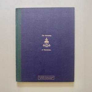 Può includere: Un libro con copertina rigida blu scuro e dorso verde. La copertina presenta il testo dorato 'The University of Manchester' sopra uno stemma. In basso, una piccola etichetta rettangolare riporta 'J.G. FELDEN, Academic Bookseller, 266, Oxford Road, Manchester.'