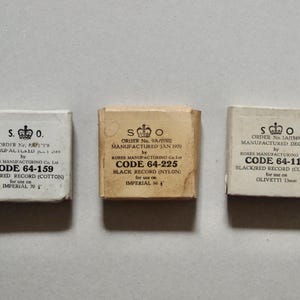 May include: Three small boxes with white labels and black text. The boxes are labeled with the text "S.O.O." and contain different types of record needles. The first box is labeled "CODE 64-159 BLACK/RED RECORD (COTTON) for use on IMPERIAL 70 1/2". The second box is labeled "CODE 64-225 BLACK RECORD (NYLON) for use on IMPERIAL 60". The third box is labeled "CODE 64-119 BLACK/RED RECORD (COTTON) for use on OLIVETTI 11mm".