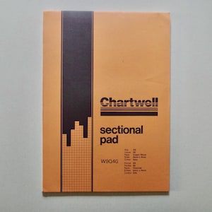 May include: An orange Chartwell sectional pad with a dark brown vertical stripe. The pad features the words "Chartwell" and "sectional pad" in black. It has a grid pattern and a series of lines and shapes, with the code W904G.