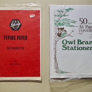 以下が含まれることがあります： 2つのタイプライター用紙のパック。赤いパックには「Silvine TYPING PAPER 50 SHEETS」と書かれています。白いパックには「50 sheets A4 Paper TYPEWRITER Owl Brand Stationery」と書かれています。どちらのパックもプラスチックで密封されています。