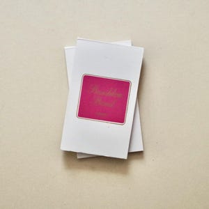 May include: A stack of white rectangular cards featuring a centred magenta label with a gold border. The text "Boulder Blend" is printed in gold script on the magenta label. The cards are arranged in a slightly offset vertical orientation.