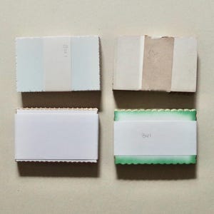 May include: Four rectangular paper items are arranged on a light beige surface. Two are white with scalloped edges, one with the text "301". The other two have color variations of blue, beige, and green.